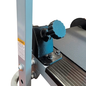 May include: Close-up of a fitness machine's adjustment mechanism. Features a teal-colored, textured knob for adjusting the machine's settings. The machine has a gray frame, black components, and a warning label.