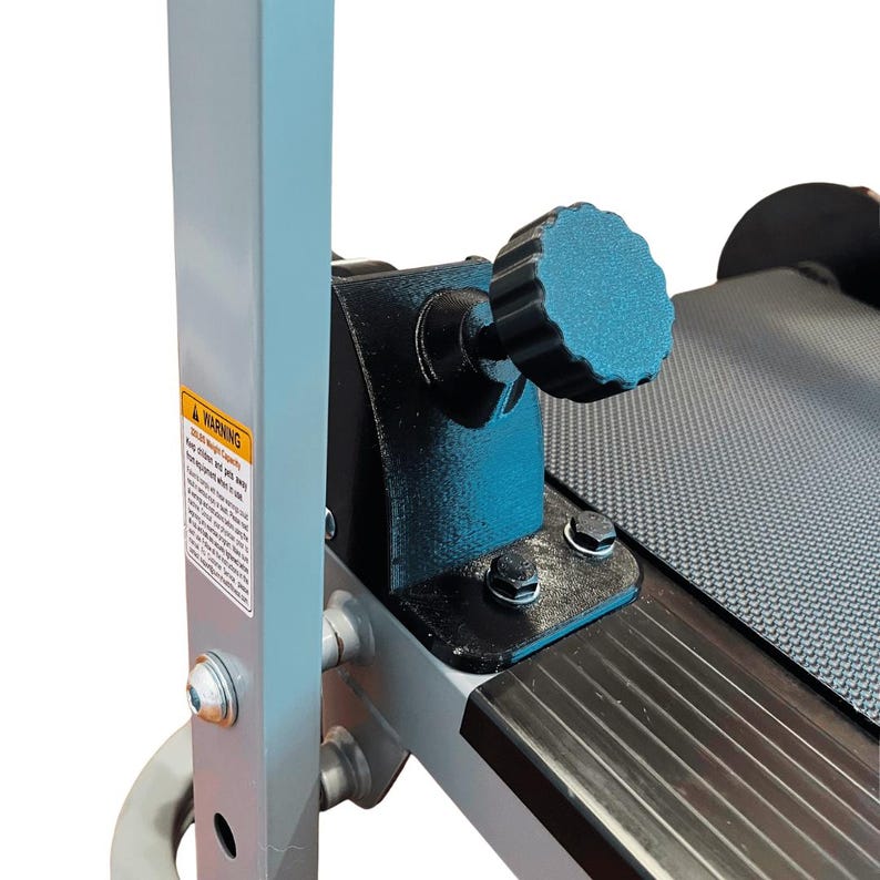 May include: Close-up of a fitness machine's adjustment mechanism. Features a teal-colored, textured knob for adjusting the machine's settings. The machine has a gray frame, black components, and a warning label.