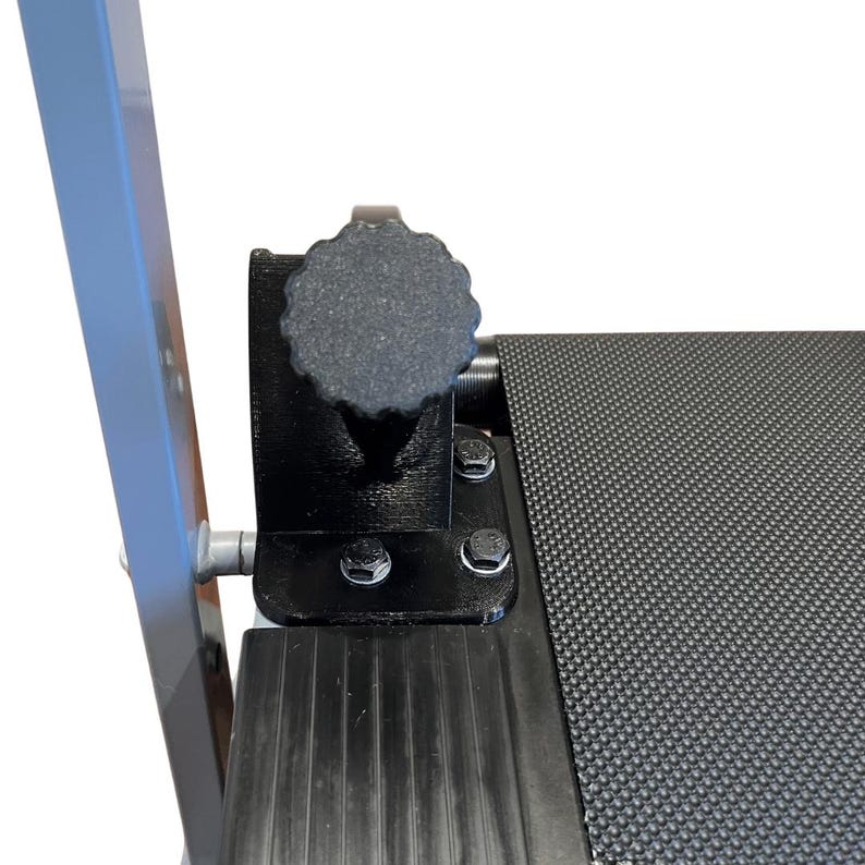 May include: Close-up of a black component with a textured, gray knob. The component is attached to a black, textured surface with silver bolts. A gray metal support is visible on the left side of the image.
