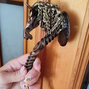 May include: A decorative bronze door handle in the shape of a horse head. The handle has a twisted design and is mounted on a wooden door. The horse head features intricate detailing and a textured mane.