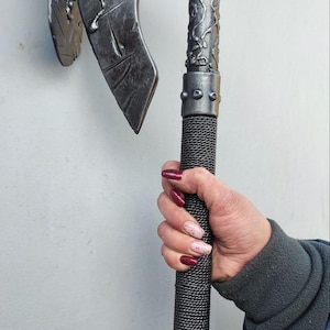 May include: A silver axe with detailed patterns on the head and handle. The axe head has a curved blade. The handle is wrapped in a textured material. The axe is held by a person. This is a decorative item or prop.