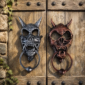 May include: Two metal door knockers shaped like horned skulls. One knocker is finished in a metallic silver color, while the other is finished in a metallic copper color. Each skull features prominent horns, hollow eye sockets, and a circular ring.