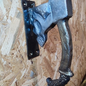 Könnte beinhalten: Ein schwarzer Metalltürgriff mit einem einzigartigen Design. Der Griff ist wie ein Ast geformt mit einem großen, quadratischen Kopf. Der Kopf hat eine strukturierte Oberfläche und einen kleinen, runden Knopf oben.