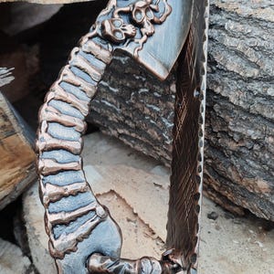 May include: A black and copper metal door handle with a skull and floral design. The handle is shaped like a curved blade with a textured grip.