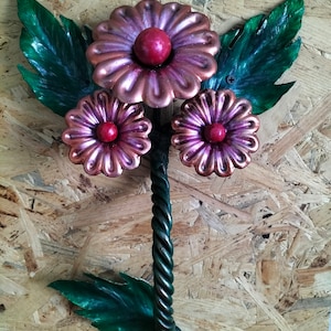 May include: A metal wall decor featuring three pink and copper flowers with red centers. The flowers are attached to a twisted metal stem with green leaves.