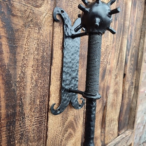 May include: Black metal door knocker with a spiked ball design. The knocker is mounted on a wooden door.