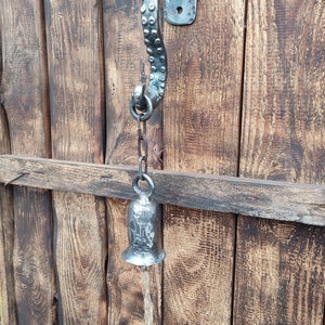 May include: A silver metal door knocker with a chain and bell hanging from it. The knocker is shaped like an octopus tentacle and is mounted on a wooden door.