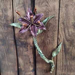 May include: A metal wall sculpture of a flower with a twisted stem and leaves. The flower is purple and has copper accents.