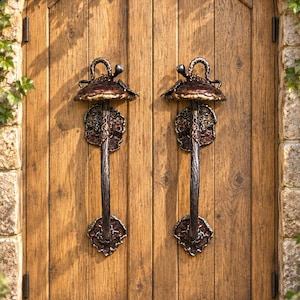 Puede incluir: Un par de puertas dobles de madera arqueadas con dos manijas de puerta metálicas oscuras en forma de hongo. Cada manija tiene un agarre texturizado similar a una rama y una parte superior ancha, montadas sobre placas metálicas irregulares.