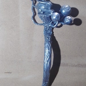 May include: A silver metal sculpture of a rabbit sitting on a branch with three round ornaments. The sculpture is made of twisted metal and has a rustic, organic look.