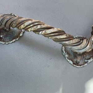 Könnte beinhalten: Verzierte Türgriff aus Bronze mit einem gedrehten Seilmotiv. Der Griff hat Eichenblatt- und Eicheldetails. Das Metall hat ein verwittertes Aussehen mit Bronze- und Grünspan-Tönen. Ein dekoratives Element.