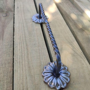 Op de afbeelding: Een zwarte metalen handdoekhouder met een gedraaid ontwerp en decoratieve bloemvormige eindkappen. De stang is gemonteerd op een houten oppervlak.