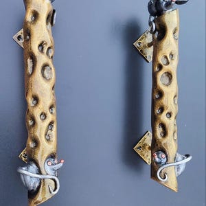 May include: Two decorative door handles with a cheese and mouse theme. The handles are made of a textured, golden-brown material with holes, resembling Swiss cheese. Each handle features a metal mouse at the top and bottom.