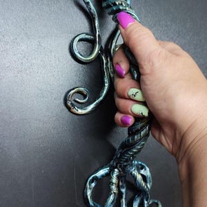 Può includere: Scultura artigianale di medusa in metallo con finitura blu e bronzo. La scultura presenta una testa a cupola e tentacoli fluenti, con dettagli intricati e una superficie strutturata. La medusa è tenuta in mano su sfondo scuro.