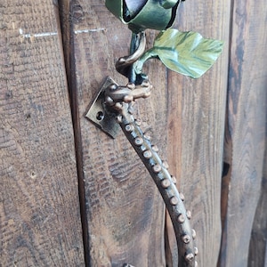 Pode incluir: Uma maçaneta de porta de metal em forma de tentáculo de polvo com uma rosa no topo. A rosa é feita de metal e é pintada em tons de marrom e verde.