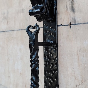 Puede incluir: Un llamador de puerta de metal negro con un diseño de cabeza de toro y un mango de metal retorcido.