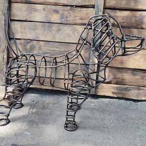 May include: A metal sculpture of a dog, made from wire and painted black. The sculpture is standing on a wooden surface.