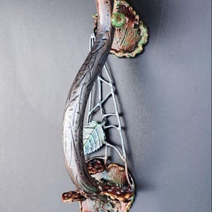 Könnte beinhalten: Ein handgefertigter Türgriff in Pilzform. Der Griff hat eine braune und weiß gepunktete Kappe, einen strukturierten Stiel und dekorative Blätter. Der Griff ist etwa 20 cm hoch.