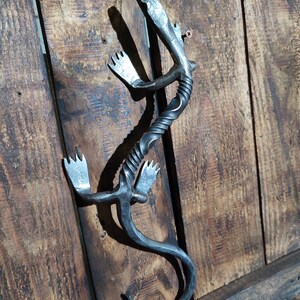 May include: A metal sculpture of a lizard, with a twisted body and detailed claws, is mounted on a wooden surface.