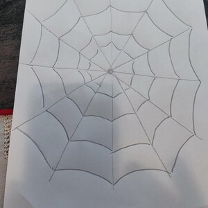 May include: A hand-drawn illustration on a white rectangular sheet of paper featuring a spider web design. The drawing consists of dark grey lines forming a radial web pattern with concentric circles connected by straight lines radiating from centre.