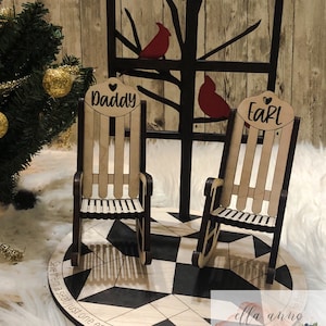 May include: A wooden rocking chair set with two chairs, a black and white checkered base, and a black silhouette of a tree with two red cardinals. The chairs are labeled "Daddy" and "Earl". The base has the text "Save them a seat, just one empty chair. You may not see them there."