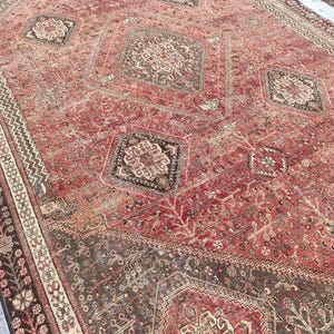 May include: A large, rectangular, distressed rug with a predominantly red and brown color palette. The rug features intricate geometric and floral patterns, with a central medallion design and a detailed border. The rug's aged appearance suggests it is vintage or antique.