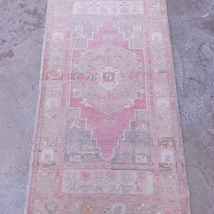 May include: Rectangular, vintage-style rug with a central pink medallion design. The rug features a faded, distressed look with a border and accents in shades of pink, beige, and gray. The rug is suitable for a living room or bedroom.
