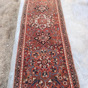 May include: An antique runner rug with a detailed floral pattern in shades of red, blue, black, and cream. The rug has a rectangular shape and a central medallion design, with intricate borders. The rug's dimensions are approximately 10 feet long.