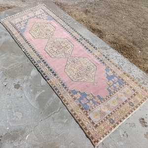 May include: A rectangular, vintage-style rug with a pink central field and intricate geometric patterns. The rug features a blue border and decorative floral motifs in beige, brown, and pink. The rug's dimensions are approximately 3 feet by 8 feet.