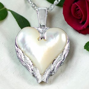 May include: A heart-shaped pendant necklace with a pearlescent center and silver-toned wing accents. The pendant hangs from a silver chain. The necklace is a piece of jewelry.