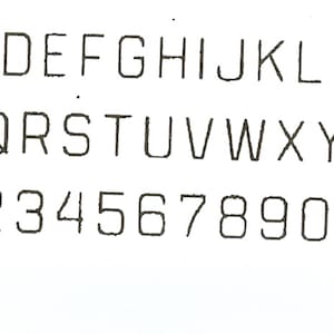May include: A white background displays the alphabet from A to Z and numbers 1 through 0. The letters and numbers are in a sans-serif font, with a slightly slanted design. The characters are black.