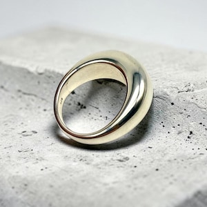 May include: A polished gold-tone ring with a thick, rounded, and smooth band. The interior of the ring band features a small, clearly visible engraving that reads 925, indicating the metal composition of this solid, circular jewelry piece.