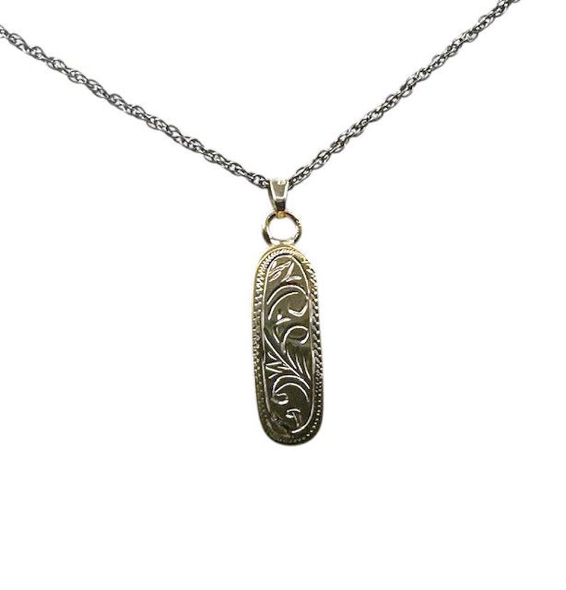 May include: A gold-colored pendant necklace with an oval-shaped pendant. The pendant features an engraved floral design and hangs from a delicate silver chain. The necklace is displayed against a white background.