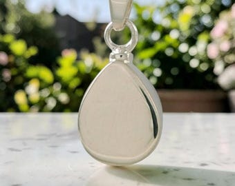 May include: A polished silver teardrop pendant suspended from a matching silver chain. The pendant features a smooth, reflective surface with a rounded bottom and a tapered top, connected to the chain by a simple, sturdy silver bail loop.