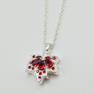 May include: A silver necklace with a red gemstone maple leaf pendant.