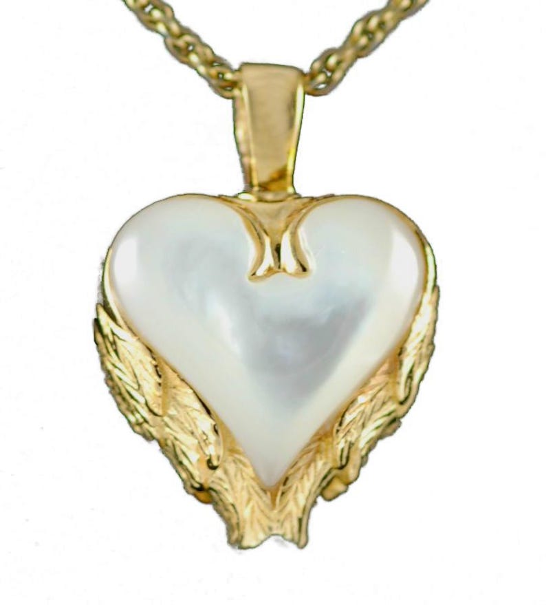 May include: A gold-toned necklace featuring a heart-shaped pendant. The pendant has a pearlescent white center, framed by a gold-colored border with a leaf design. The chain is also gold-colored.