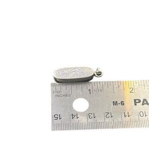May include: Silver pendant with an engraved floral design. The pendant is oval-shaped and measures approximately 1 inch in length. It has a small loop at the top for a chain. The pendant is shown next to a ruler.