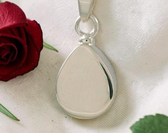 May include: A silver-toned teardrop-shaped pendant suspended from a matching silver-toned chain. The pendant features a smooth, polished, reflective surface with a simple bail connecting it to the chain, presented alongside a deep red rose.