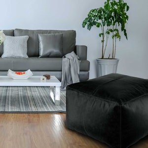 May include: A modern living room scene featuring a gray sofa, white coffee table, and a black square ottoman. A terracotta vase with white flowers sits on the table. A potted plant adds a touch of greenery.