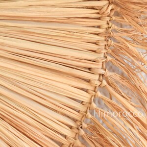 Pu&ograve; includere: Primo piano di un cappello di paglia intrecciata, che mostra la trama naturale e le calde tonalit&agrave; beige del materiale. Il bordo del cappello &egrave; cucito saldamente, con un dettaglio a frange. L'immagine include il testo "Himorocco".