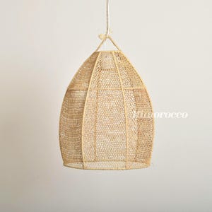 May include: A natural woven pendant light fixture with a round, dome-shaped shade. The shade is made of a light brown, woven material with a delicate, open weave.