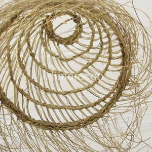 May include: A close-up of a woven, circular, straw lampshade with a natural, light brown color. The lampshade is made of thin, braided strands of straw, creating a delicate and airy appearance.