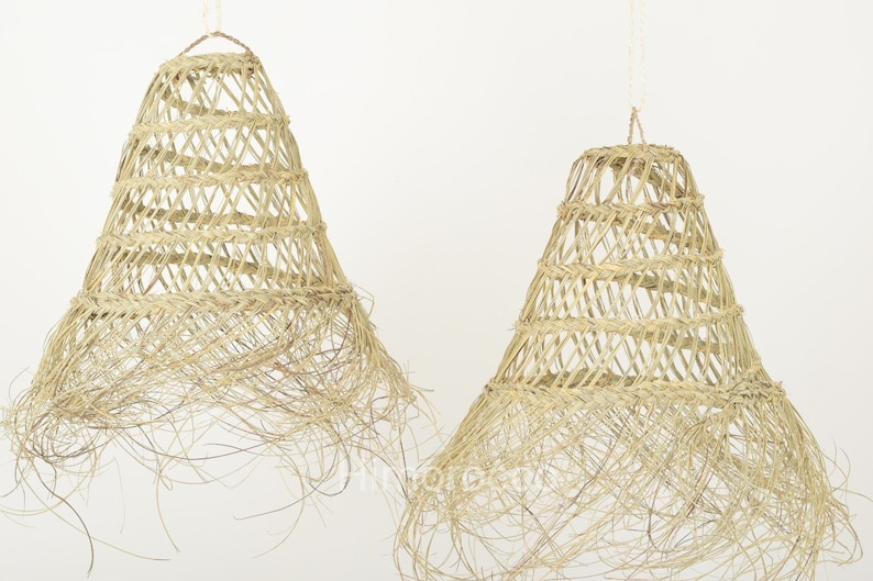 May include: Two natural woven pendant light shades with a fringe detail. The shades are made of natural materials and have a rustic, bohemian style.