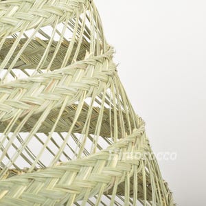 May include: A close-up of a woven lampshade made of natural materials. The lampshade is a spiral shape with a light beige color.
