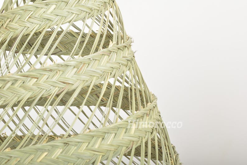 May include: A close-up of a woven lampshade made of natural materials. The lampshade is a spiral shape with a light beige color.