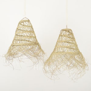 May include: Two natural woven pendant lights with a fringe detail. The lights are made of a light brown material and have a bell shape.