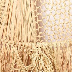K&ouml;nnte beinhalten: Nahaufnahme einer gewebten Makramee-Wandbeh&auml;nge mit Fransenrand. Die Beh&auml;nge ist aus Naturfasern gefertigt und hat eine hellbeige Farbe.
