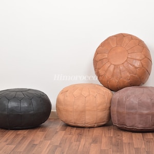 Könnte beinhalten: Vier Lederpoufs in verschiedenen Farben: Schwarz, Braun und zwei Brauntönen. Die Poufs sind rund und haben ein gestepptes Design.