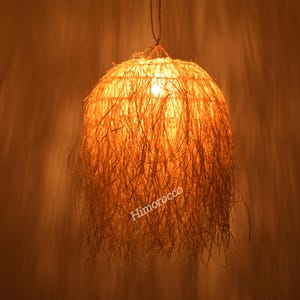 Könnte beinhalten: Eine runde, geflochtene Pendelleuchte aus einem natürlichen, strohähnlichen Material. Die Leuchte ist eingeschaltet und strahlt ein warmes Licht aus.
