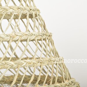 May include: A close-up of a woven lampshade made of natural materials. The lampshade is a light beige color and has a geometric pattern.